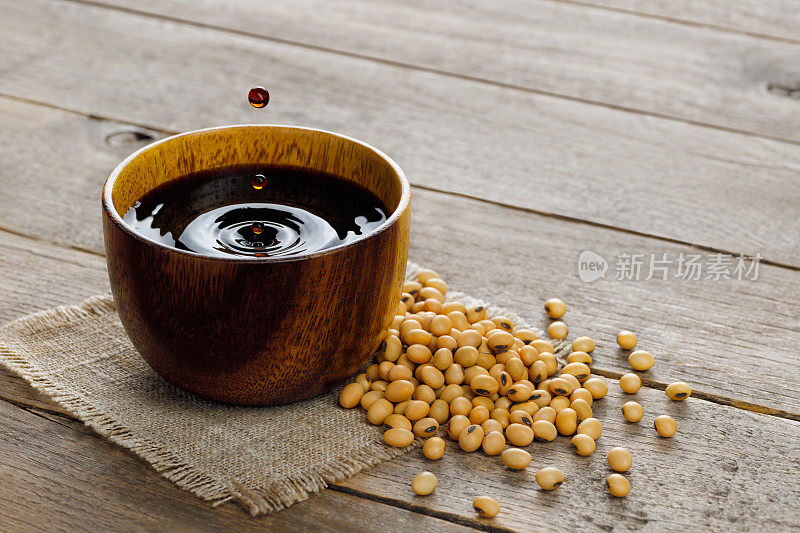 soy sauce in bowl with falling drops and dry soybeans on table